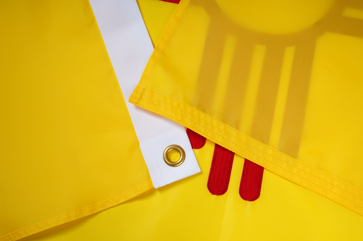 Close-up of the New Mexico State Flag by Flag Stars Inc shows durable yellow fabric, stitched edges, a white strip with metal grommet, and red shapes—100% made in the USA for outdoor use.