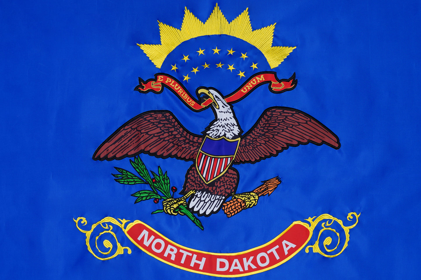 The Flag Stars Inc North Dakota State Flag features a bald eagle with "E Pluribus Unum" and "North Dakota" on blue, adorned with raised embroidery for outdoor use. 100% made in the USA.