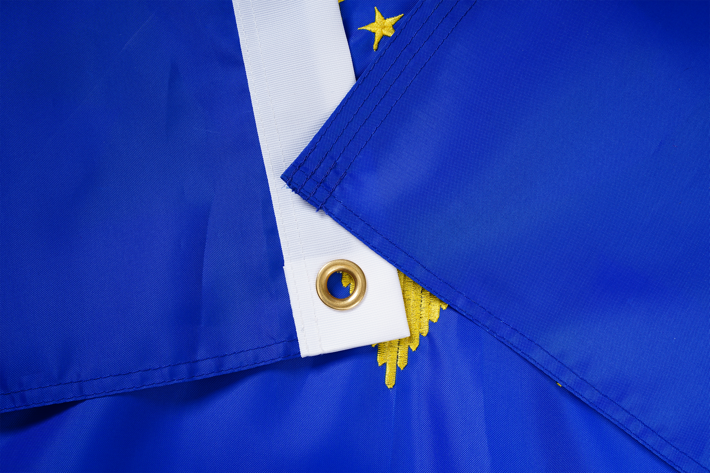 Close-up of two North Dakota State Flags by Flag Stars Inc, featuring gold grommets, yellow stars, and raised embroidery. Crafted for outdoor use and 100% made in the USA.