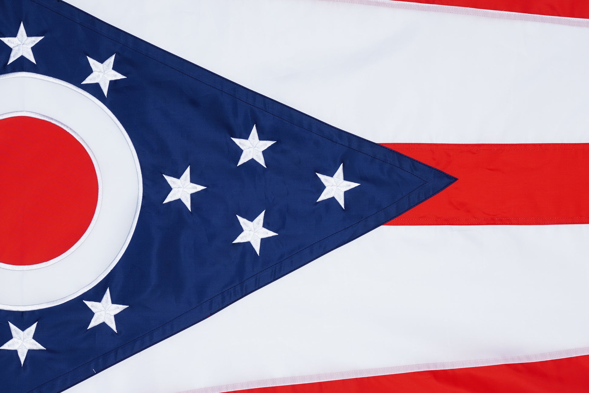 The Ohio State Flag - 100% Made in USA by Flag Stars Inc features red and white stripes, a blue chevron with white stars, and a red and white circle, designed for durable outdoor display.