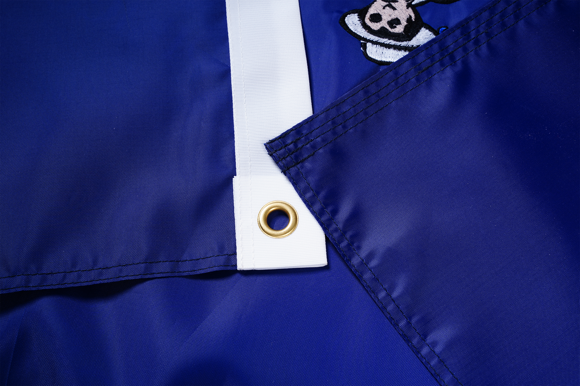 Close-up of the Maine State Flag by Flag Stars Inc—crafted in the USA from blue nylon with a white reinforced edge, brass grommet, and part of a cartoon character visible in the top right corner; designed for outdoor use.