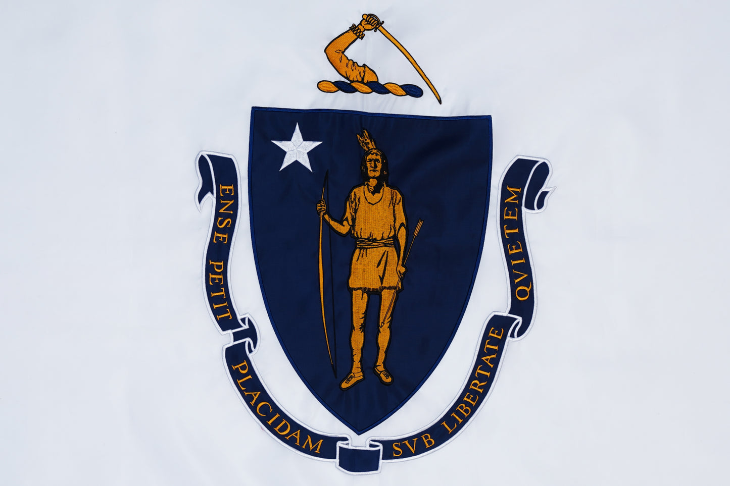 The Massachusetts State Flag by Flag Stars Inc, 100% made in USA, displays a blue shield with a Native American figure, white star, bent arm with sword above, and a Latin motto banner encircling the shield.
