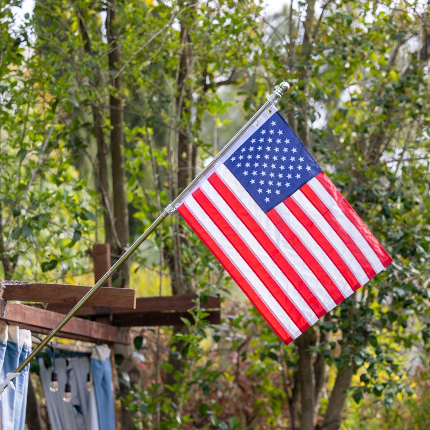 A The FlagStars 2' X 3' AMERICAN FLAG on a pole waves outdoors with greenery and trees in the background, promising long-lasting pride.