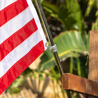 A close-up of an American flag on a 6 FT ALUMINUM FLAG POLE WITH TANGLE FREE SPINNERS by The FlagStars, with the red and white stripes visible. The background is blurred greenery.