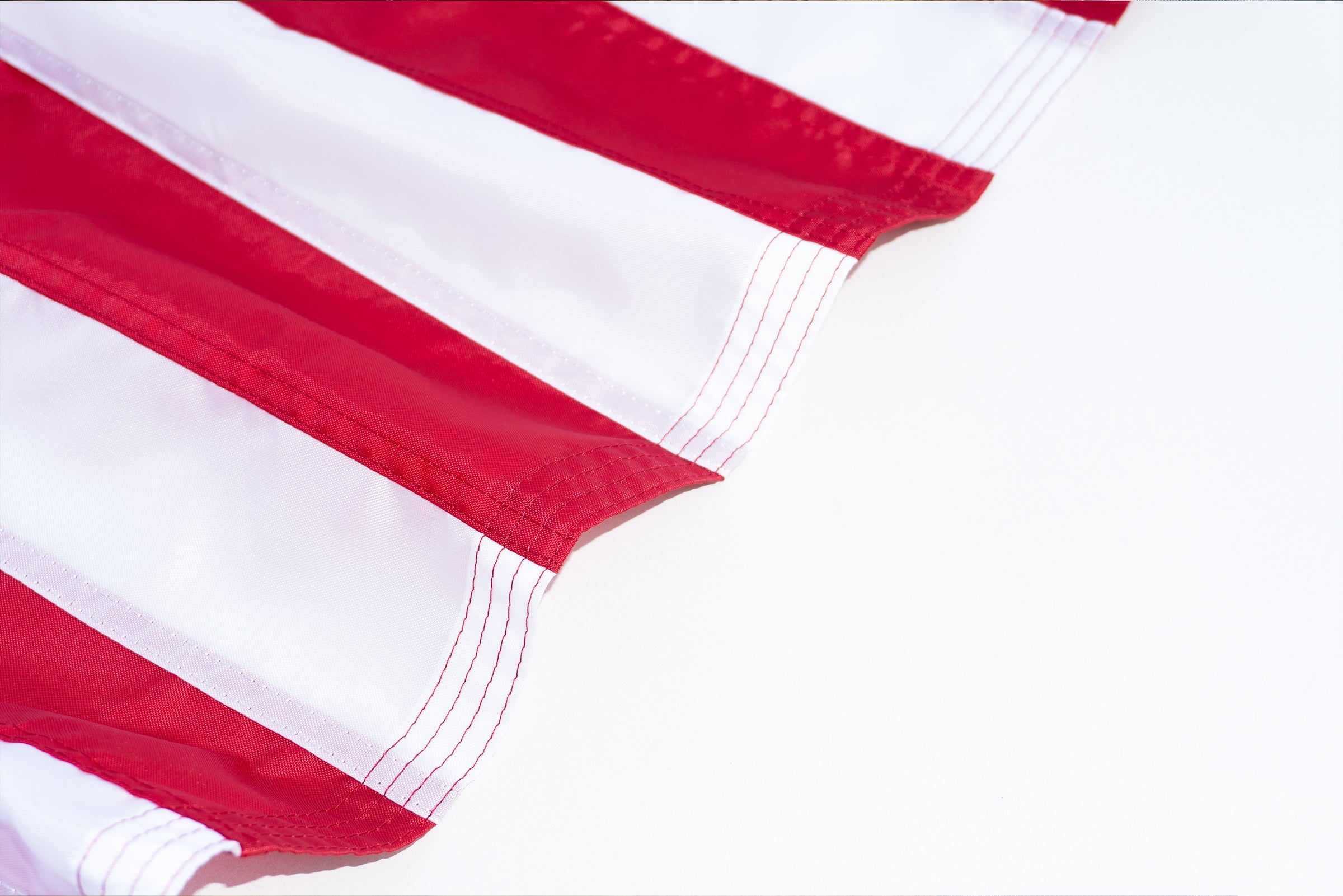 Close-up of red and white striped fabric, likely part of an American Flag, with stitching details visible.