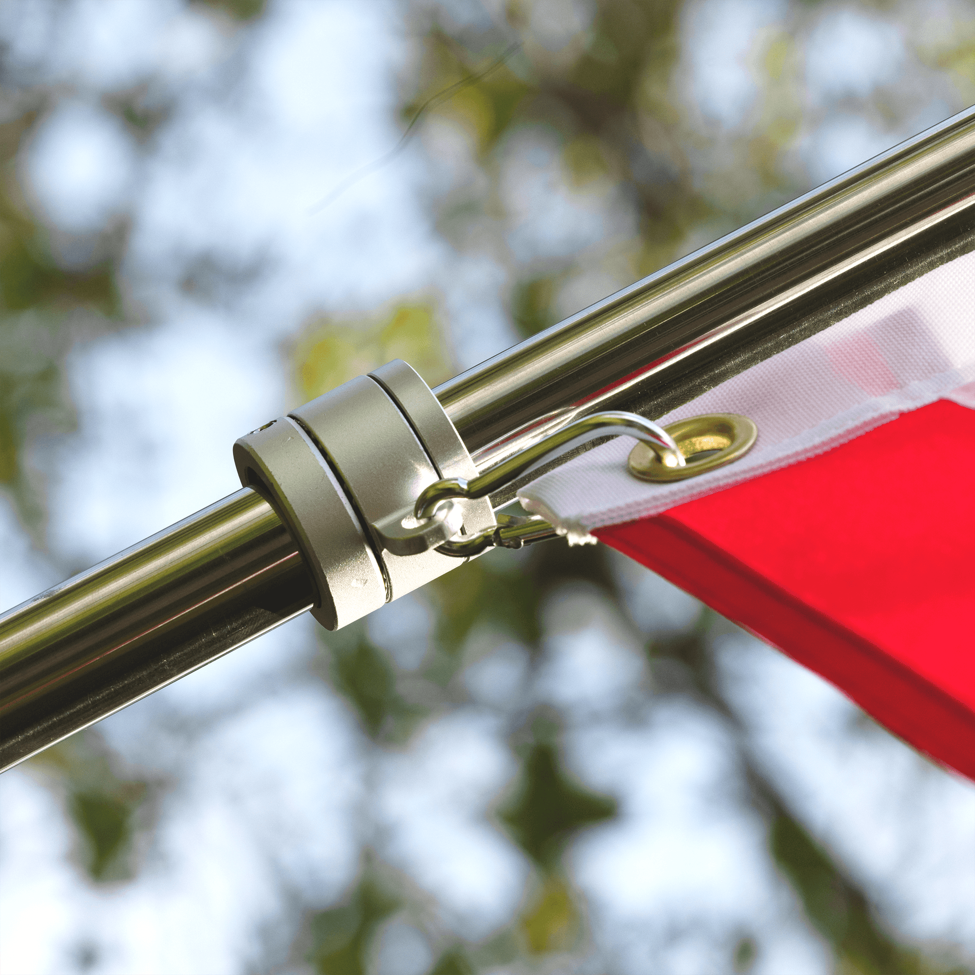 Close-up of a flagpole attachment holding a red and white flag, with a blurred background of tree branches and sky. The 6 FT ALUMINUM FLAG POLE WITH TANGLE FREE SPINNERS by The FlagStars features tangle-free spinners for easy installation.
