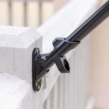 A close-up of a black metal FLAG MOUNTING BRACKET by The FlagStars secured to a white wooden post with screws, holding a rod at an angle. Proudly made in the USA, this sturdy bracket ensures long-lasting durability.