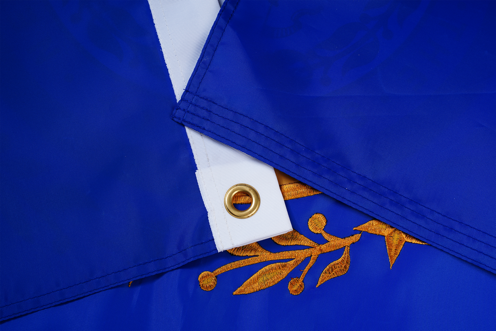 Close-up of two overlapping New Hampshire State Flags by Flag Stars Inc, 100% Made in USA, showing blue fabric with a white strip, brass grommet, and gold raised embroidery branch motifs. Designed for outdoor use.