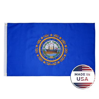 Flag Stars Inc’s New Hampshire State Flag – 100% Made in USA – features a blue background with the state seal, shown beside a round “Made in USA” American flag label. Built durable for outdoor use.