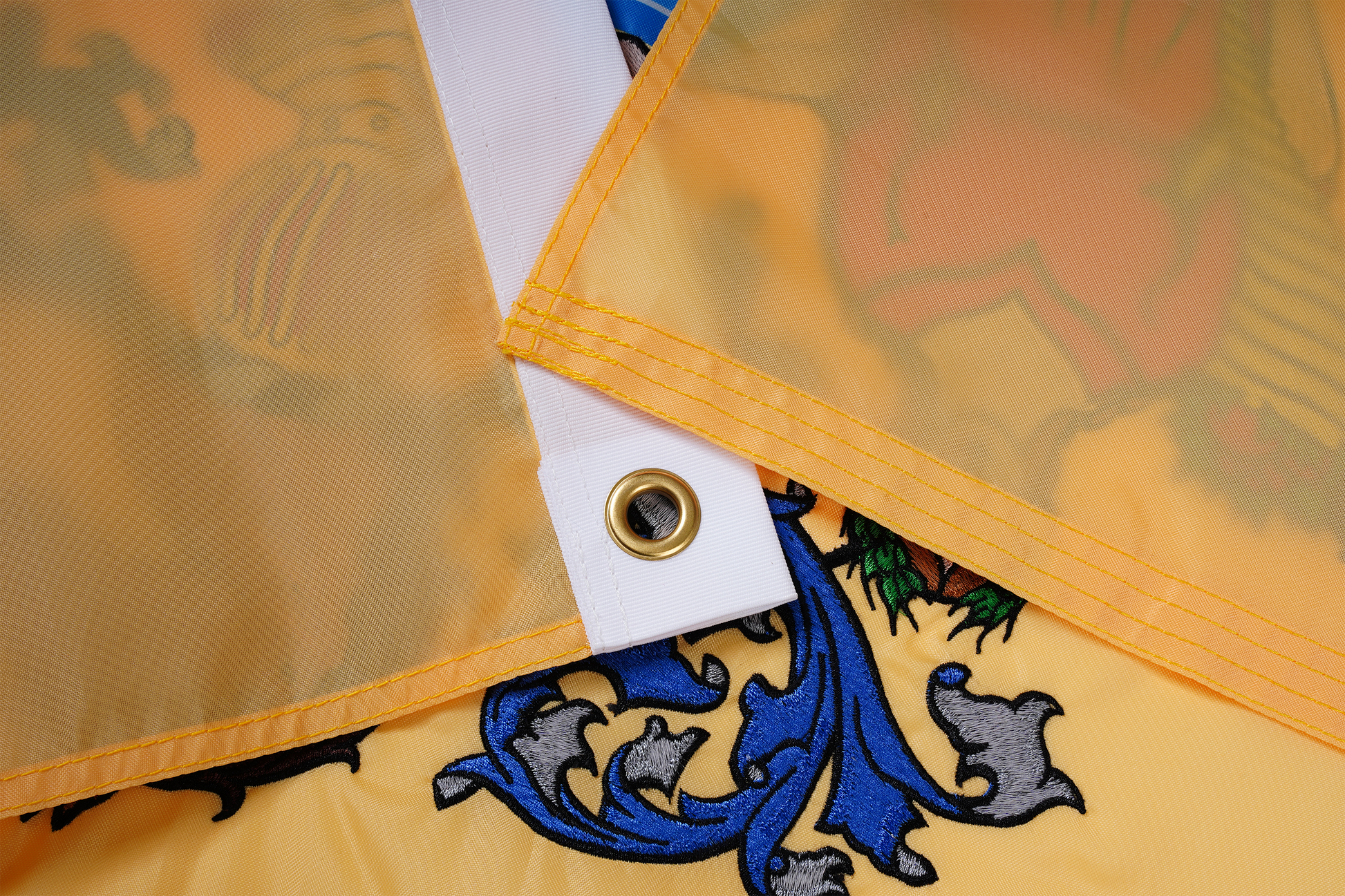 Close-up of the New Jersey State Flag by Flag Stars Inc, showing a yellow corner with metal grommet and colorful raised embroidery—100% made in USA, ideal for outdoor use.