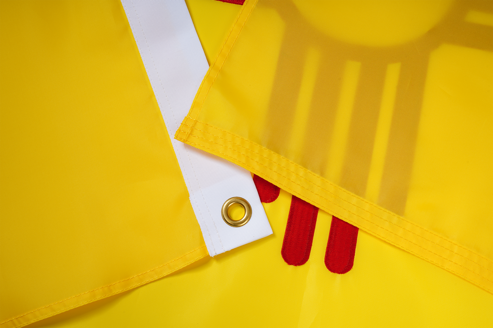 Close-up of the New Mexico State Flag by Flag Stars Inc shows durable yellow fabric, stitched edges, a white strip with metal grommet, and red shapes—100% made in the USA for outdoor use.