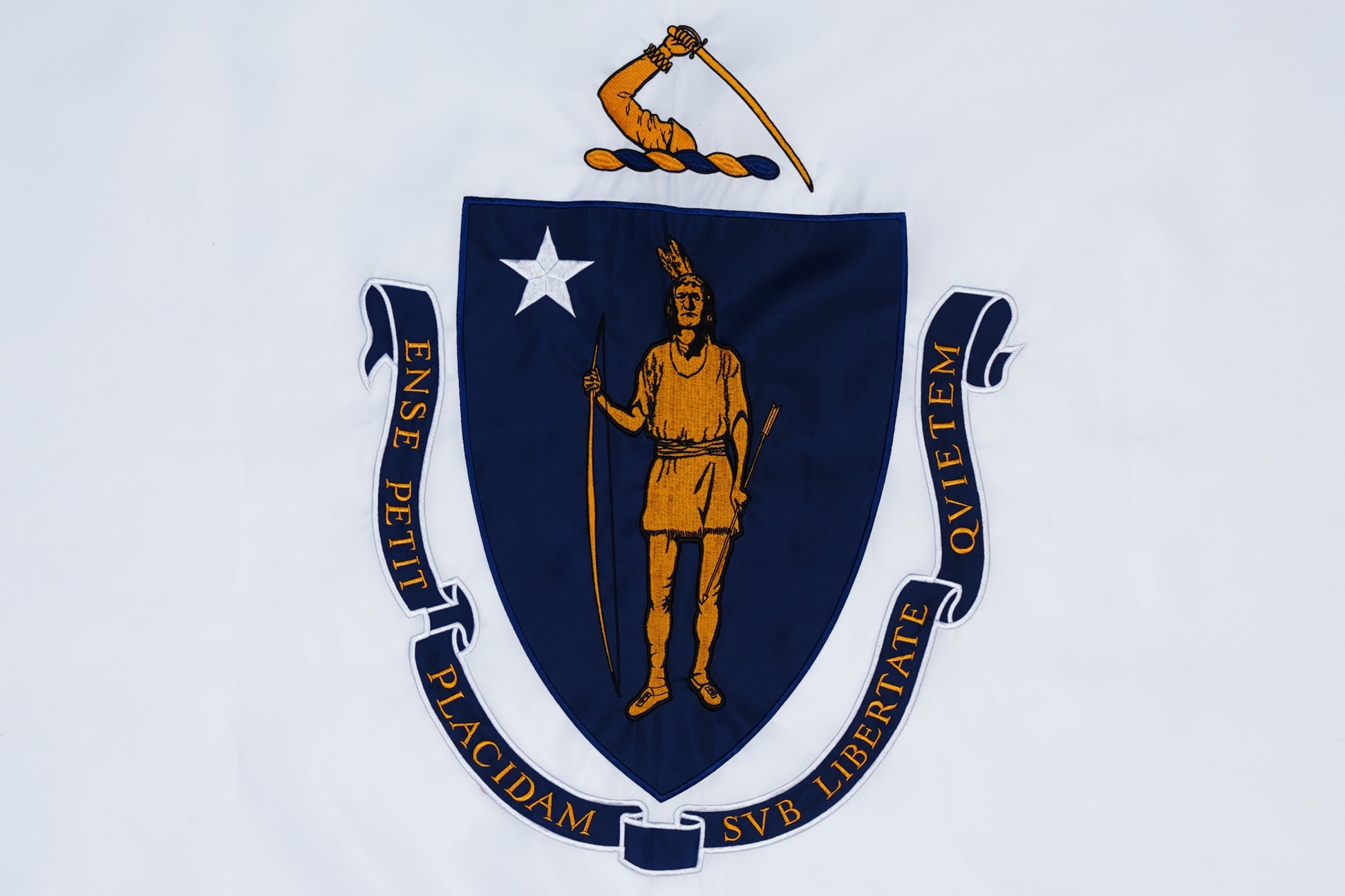 The Massachusetts State Flag by Flag Stars Inc, 100% made in USA, displays a blue shield with a Native American figure, white star, bent arm with sword above, and a Latin motto banner encircling the shield.