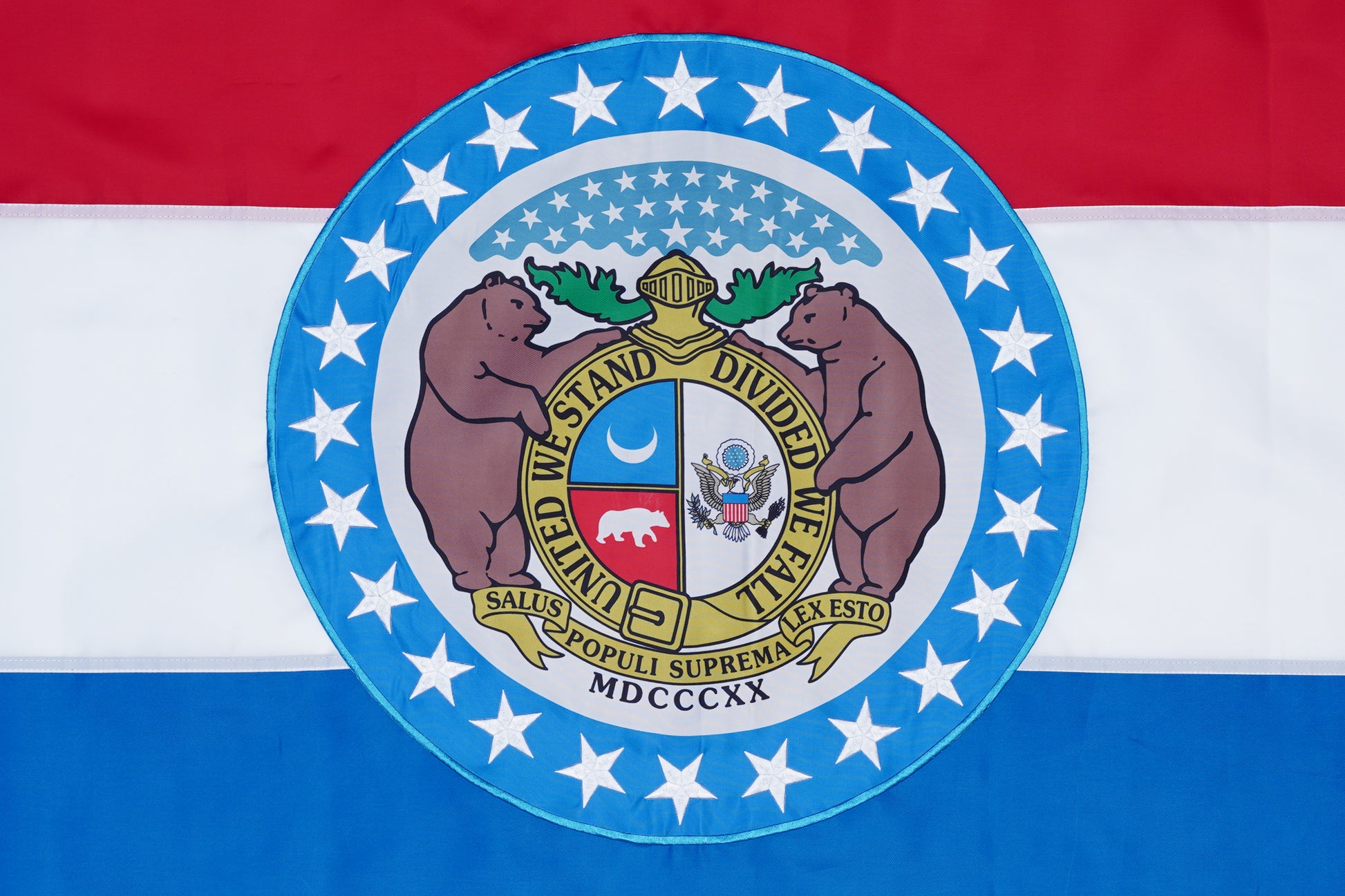 The Missouri State Flag - 100% Made in USA by Flag Stars Inc features red, white, and blue stripes, the state seal at the center flanked by two bears, all encircled by a ring of stars.