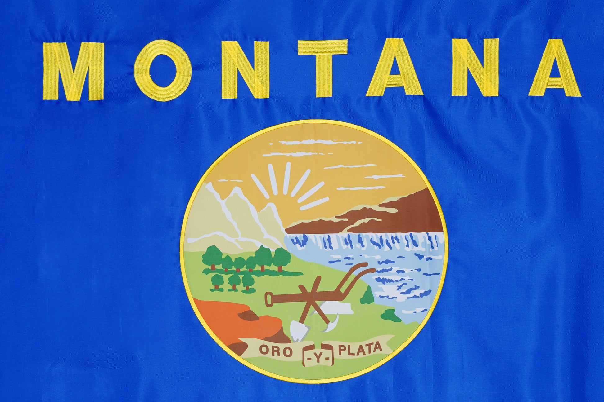 The Montana State Flag by Flag Stars Inc features a blue background, "Montana" in yellow, the state seal with mountains and "Oro y Plata," crafted with raised embroidery for outdoor use—100% Made in USA.