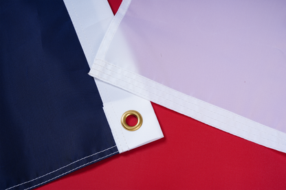 Close-up of two nylon North Carolina State Flag corners with metal grommets by Flag Stars Inc—one dark blue, one white—on a red surface. 100% Made in USA and outdoor ready.