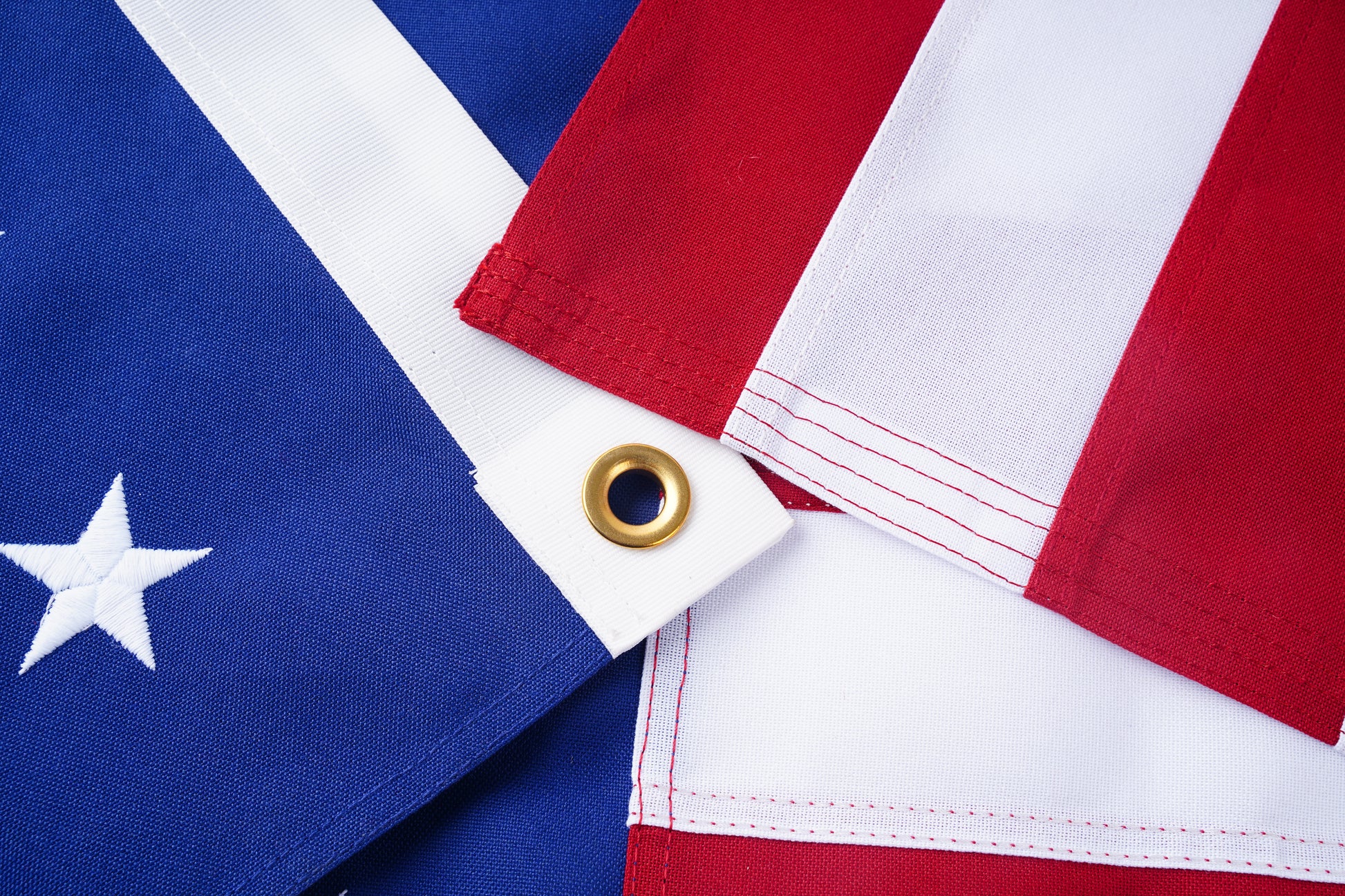 Close-up of the Spun Poly American Flag by Flag Stars Inc—100% Made in USA—shows blue with white stars, vivid red and white stripes, brass grommet, and UV resistant fabric for long-lasting color.