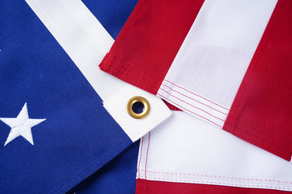 Close-up of the Spun Poly American Flag by Flag Stars Inc—100% Made in USA—shows blue with white stars, vivid red and white stripes, brass grommet, and UV resistant fabric for long-lasting color.