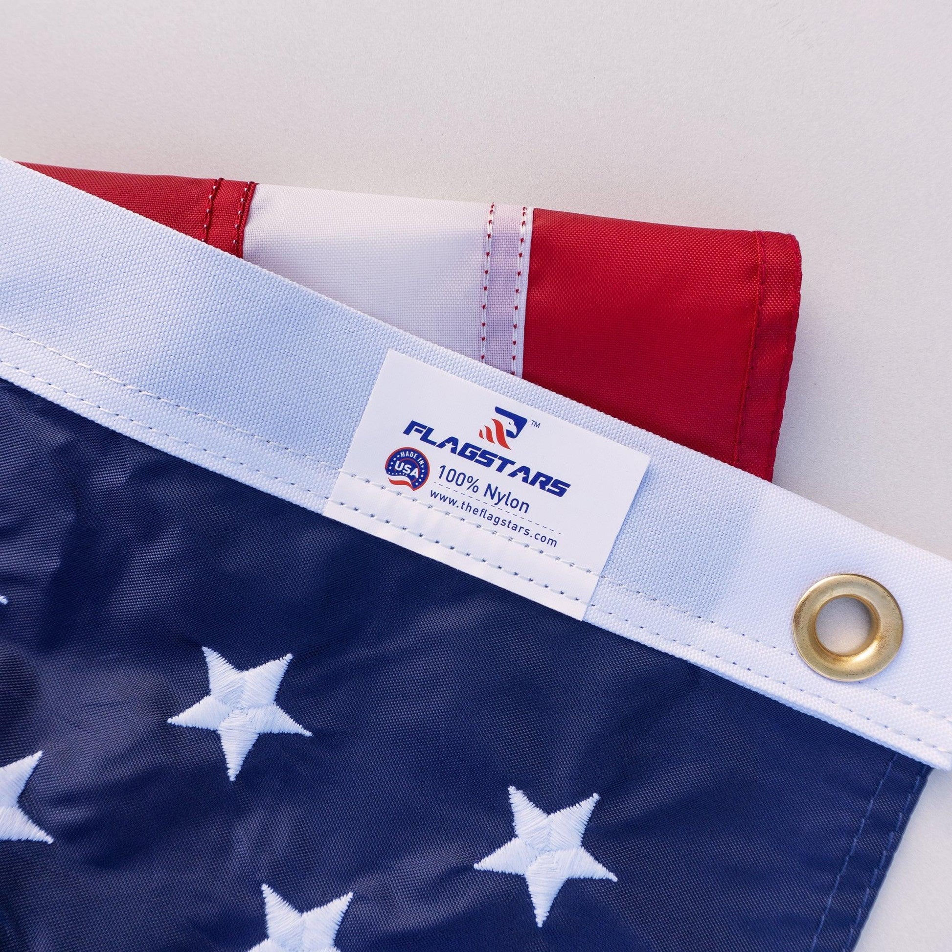 Close-up of the corner of a long-lasting 2.5' X 4' AMERICAN FLAG made by The FlagStars, showing the label, eyelet, and parts of the stars and stripes—proudly made in the USA.