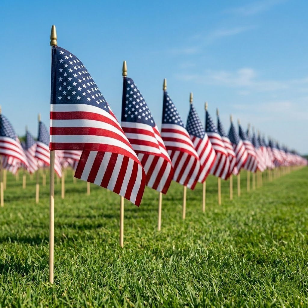 Rows of Flag Stars Inc Poly Cotton US Stick Flags with natural wood sticks, made in the USA, stand arranged in the grass under a clear blue sky, creating a striking patriotic display.