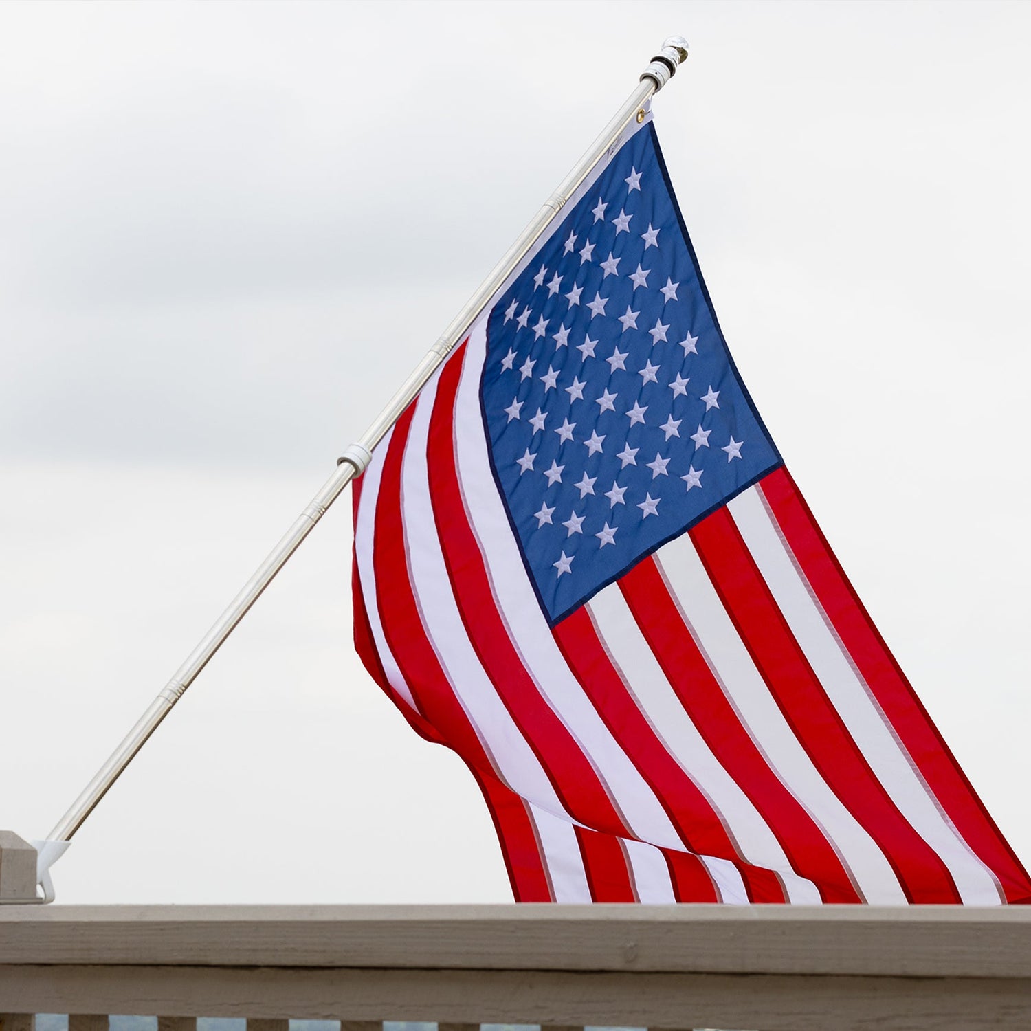 An American flag, hand made with precision and care, is displayed on a pole against a cloudy sky backdrop.