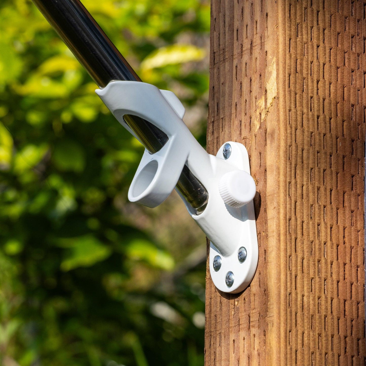 A white FLAG MOUNTING BRACKET from The FlagStars, hand made and mounted on a wooden post, stands proudly with an American flag against a green, blurred background.